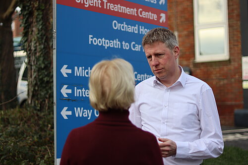 James MacCleary talking to a constituent next to an NHS signboard